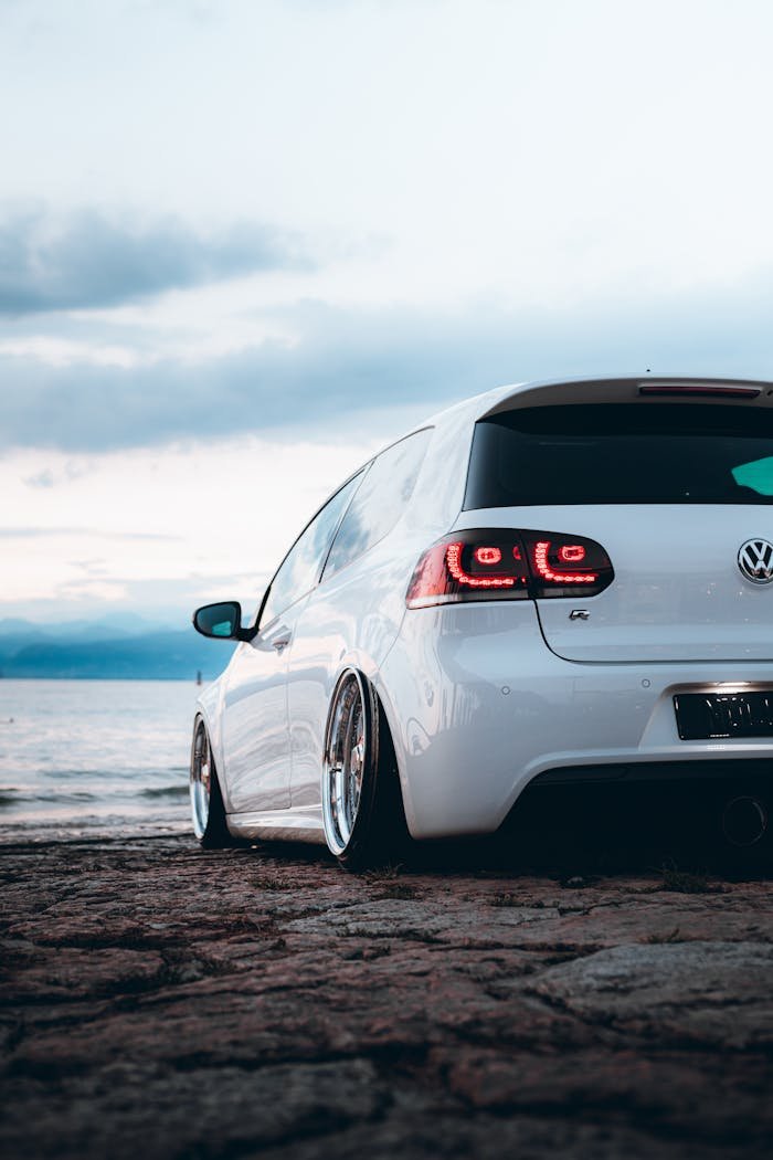 A white Volkswagen rests near the ocean with dramatic skies at twilight.